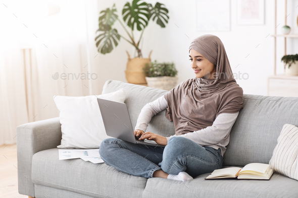 Remote Business. Happy Arabic Businesswoman Working With Laptop And Documents At Home, Sitting On Comfortable Couch At Home