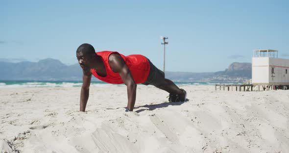 Focused african american man doing press ups on the beach, exercising outdoors by the sea alt