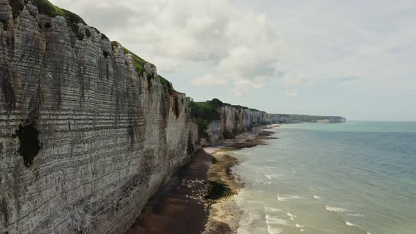 The Drone Flies at the Foot of Sheer Striped Cliffs with a Pebbly Shore alt