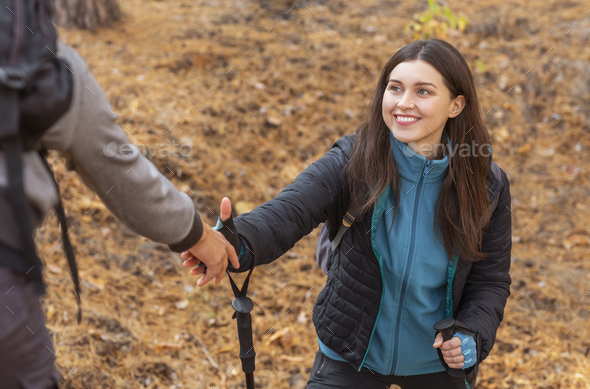 Cheerful girl taking helping hand from guy while hiking at countryside, closeup