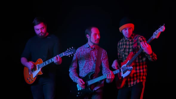 A Trio of Guitarists Perform the Composition on Their Instruments in the Studio Against a Black alt