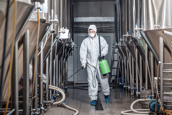 Startup and small business. Man working in brewery factory in protective suit and mask disinfects plant during quarantine, free space