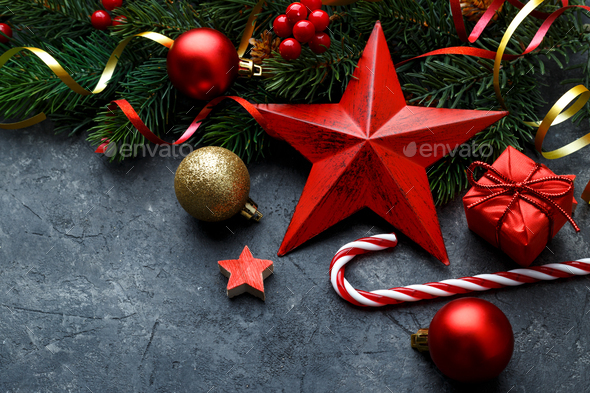 Christmas flat lay with red star, gold ornaments and fir tree branch on black stone background with copy space