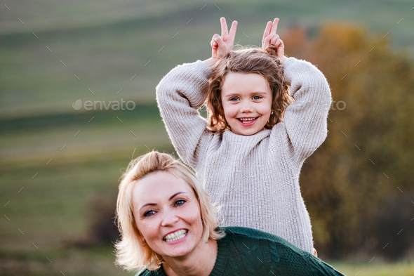 Portrait of small girl with mother on a walk in autumn nature, having fun.