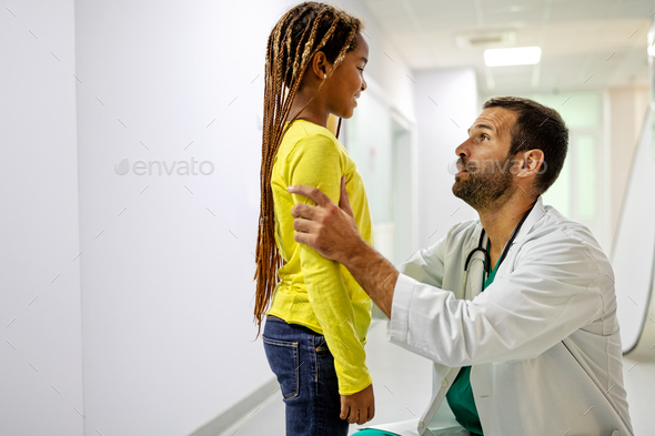 Handsome doctor having conversation with sad little girl at the hospital. Doctor consoling child
