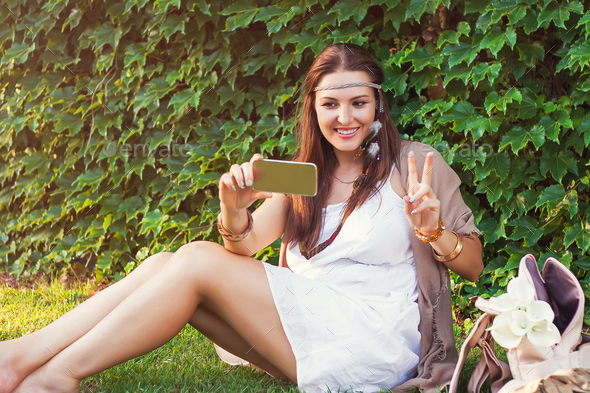 Young woman sitting on grass next green wall and having video chat on smartphone