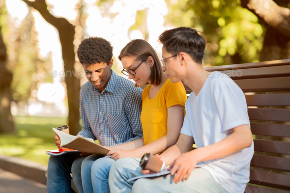 Three Diverse Students Learning Sitting On Bench Outdoors In University Campus. Higher Education Concept