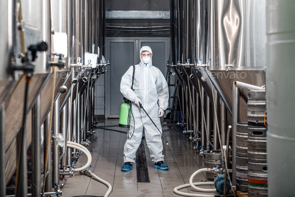 Young man working in beer manufacturing factory in protective suit and cleans up during epidemic, free space