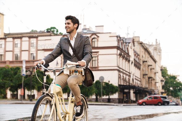 Image of a handsome smiling business man outdoors walking on a bicycle looking aside