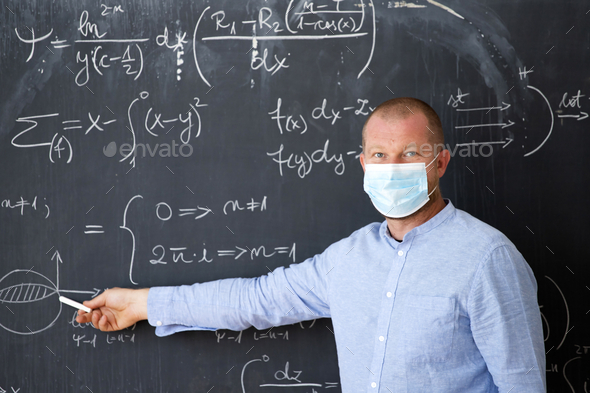 Male teacher with mask teaching math lesson at school. Social distanting and classroom safety during coronavirus epidemic