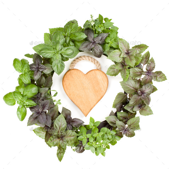 Various sweet basil herb leaves round frame with wooden heart shaped board in the centre