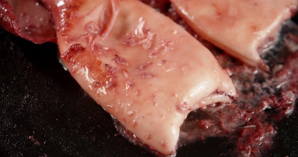 The Squid Is Fried in a Frying Pan with Bubbles of Oil.  alt
