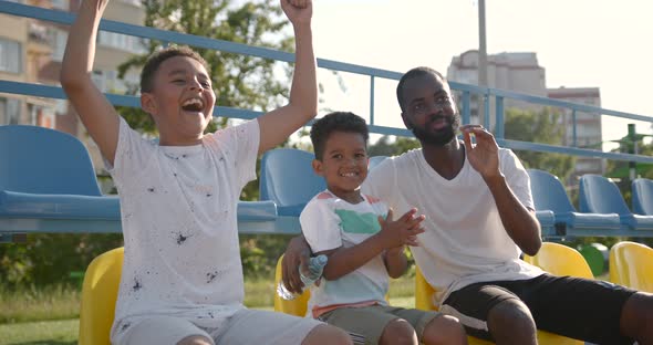 Black Father and Two His Multiracional Sons Watching Football Game on Stadium alt