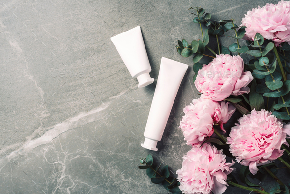 Cosmetic cream bottle, pink peony flowers, eucalyptus flower, copy space on marble background. Blank label for branding mock-up. Flat lay. Beauty products. Skin care, body treatment, spa concept.