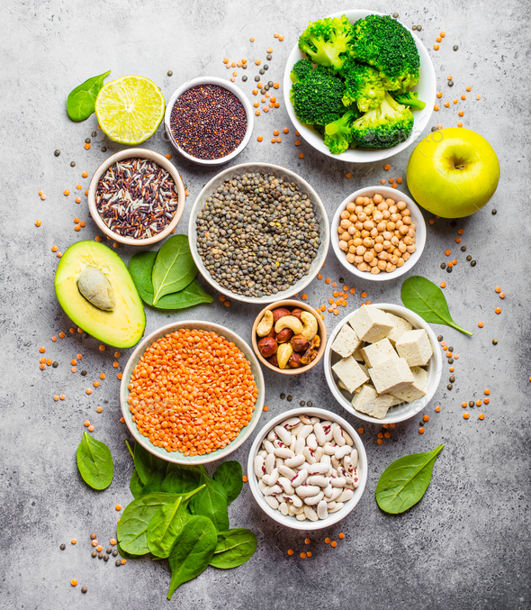 Variety of nutrient-rich food for vegans: beans, lentils, quinoa, tofu, vegetables, nuts, chickpeas, rice, avocado, fruit, stone rustic background, top view. Healthy balanced vegetarian nutrition