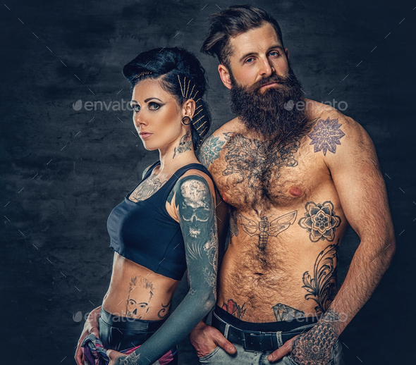 Studio portrait of full body tattooed couple over dark grey background.