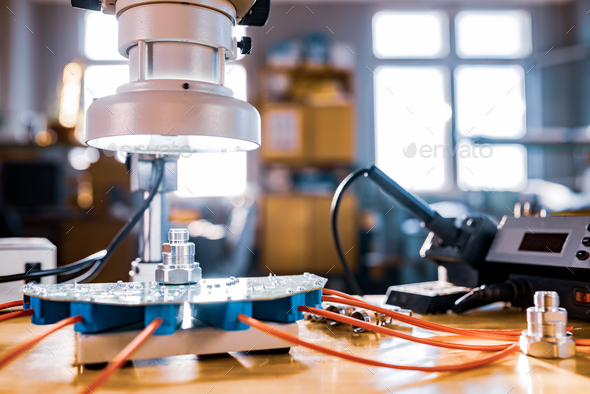 Modern microscope, connectors component and large green microcircuit in workshop laboratory - Stock Photo - Images