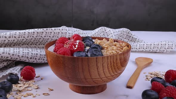Pouring Honey on Yogurt with Oat Flakes and Berries