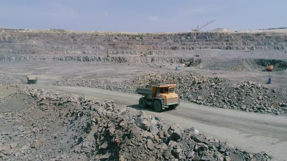 Mining Dump Trucks in Large Granite Open Pit Mine. Loaded Truck Rides on Road Quarry Ledge Aerial alt