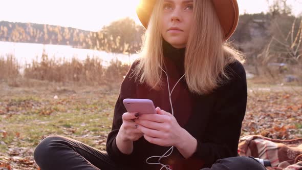 Slow Motion Caucasian Blonde Woman with Beige Hat in Black Sweater Use Phone and Listen Music alt