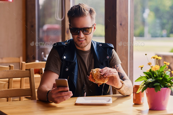 Attractive hipster dressed in leather jacket eating a vegan burger.