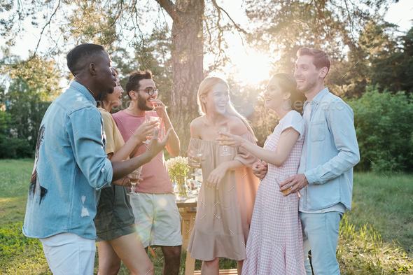 Young joyful friends with drinks laughing at funny stuff told by one of them