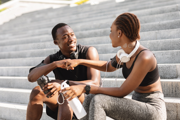 Good Job Partner. Black Athlete Guy And Girl Fist Bumping After Training Outdoors, Sitting On Urban Steps, Resting After Workout In Park, Closeup