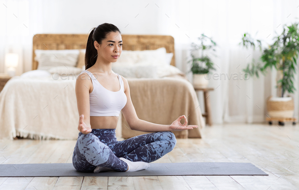 Happy young chinese woman sitting yoga pose and watching