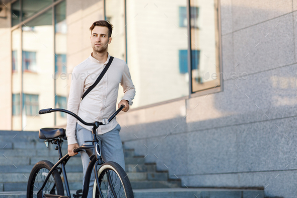 Convenient way to travel. Handsome businessman in formal clothes going to work by bike at city in daylight at autumn