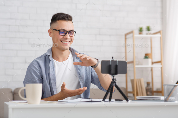 Work and study online during self-isolation. Man in glasses gestures and looks at camera of smartphone in interior of living room