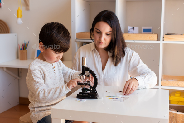 Lillte Kid exploring science with a microscope and mother or teacher help. Homeshooling. Learning Community. Montessori School