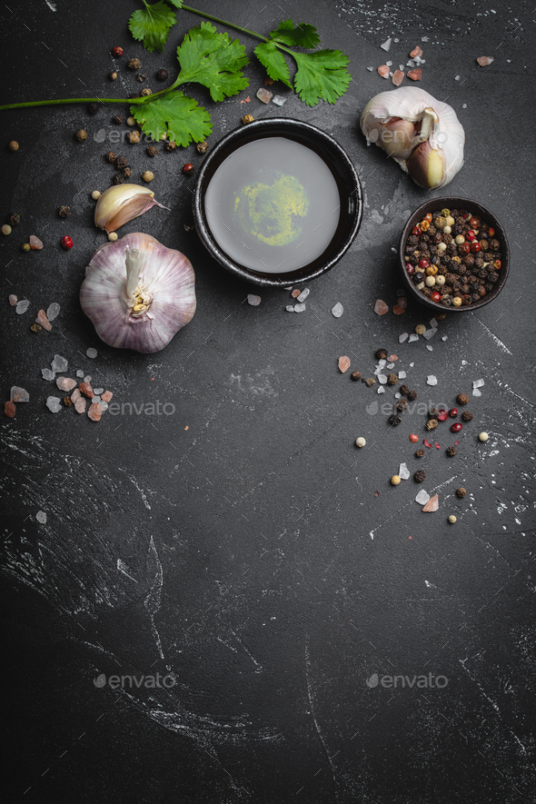 Close up of traditional cooking ingredients: garlic, olive oil, salt, pepper, fresh herbs on dark rustic background. Food frame, concept for cooking healthy food with space for text, top view