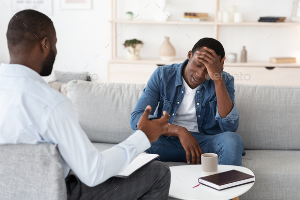 Psychotherapy Concept. Depressed black man talking to psychologist during individual therapy, therapist advising something