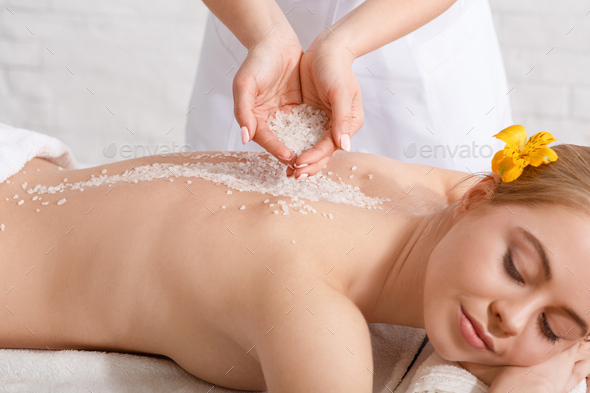 Scrub effect in spa procedure. Hands of professional doing massage with salt for woman with closed eyes on table, cropped