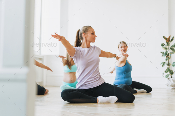 Group of pregnant women in sports uniforms with coach doing gymnastic in bright studio