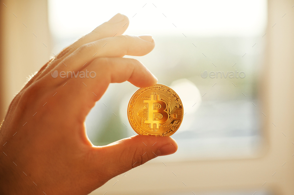 Hand holding shiny golden bitcoin in light, gold money