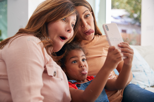 Multi-Generation Female Hispanic Family At Home Pulling Funny Faces For Selfie On Mobile Phone