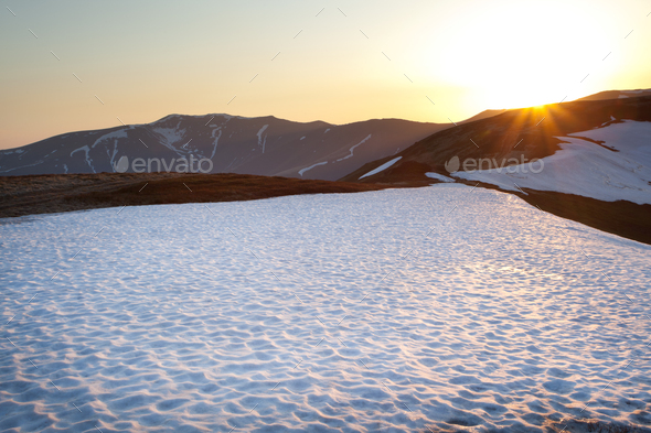 Beautiful landscape mountain with snow and grass, sunny weather. Mountains on background, sun shining in camera