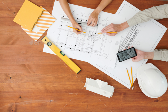 Top view of hands of two architects pointing at blueprint during discussion - Stock Photo - Images