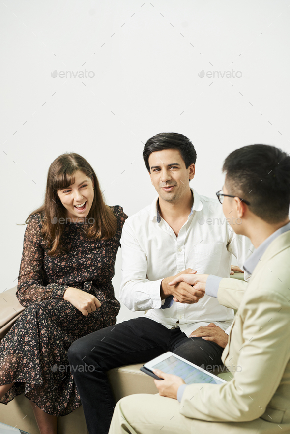 Smiling couple have a talk with financial adviser and shaking hands after consultation at office