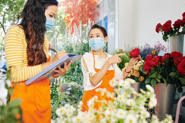 Team of florists in medical masks discussing which flowers to order for the next week and filling document
