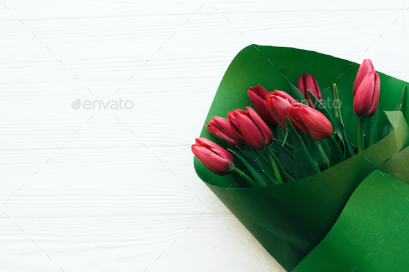 Beautiful red tulips bouquet in green paper on white wooden background - Stock Photo - Images