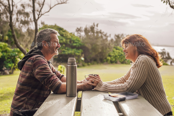 Middle-aged couple sitting on the benches with table in park and drinking tea. - Stock Photo - Images