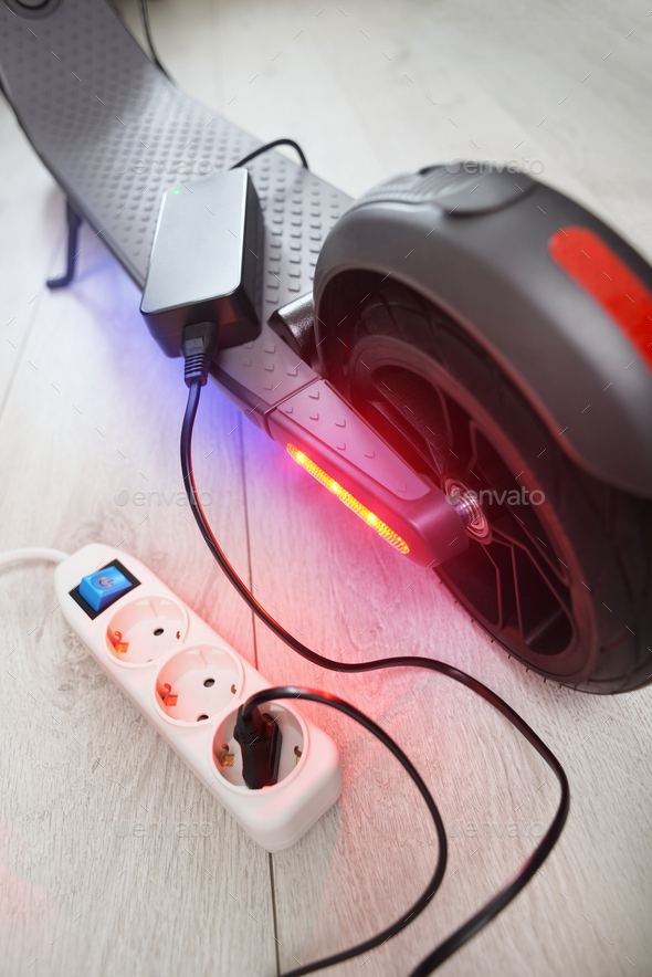 Battery charging process of electric motorized scooter. Stock Photo by
