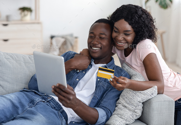 Happy married black couple with digital tablet and credit card buying furniture online, home interior, empty space