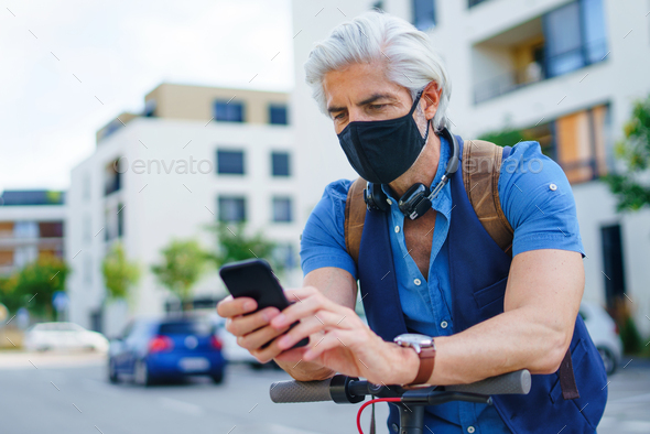 Mature man commuter with face mask and telephone outdoors in city, coronavirus concept - Stock Photo - Images