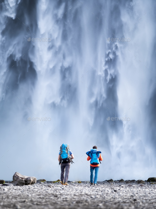 Iceland. Travelers couple look at the Skogafoss waterfall. - Stock Photo - Images