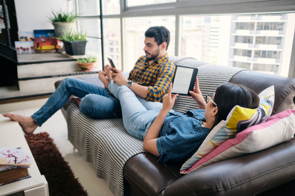 Young Couple Reading Ebook With Ereader On Couch - Stock Photo - Images