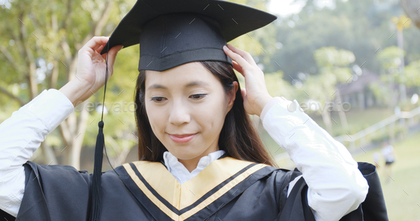 Woman adjusting her graduation gown and mortarboard in campus - Stock Photo - Images