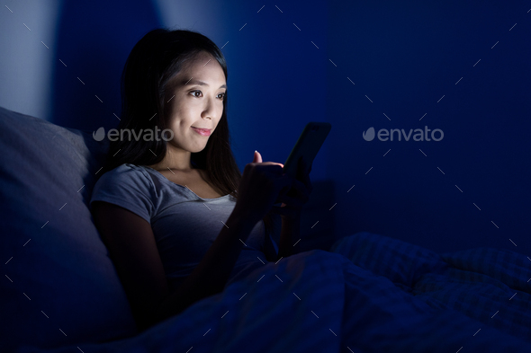 Woman using mobile phone on bed at night - Stock Photo - Images